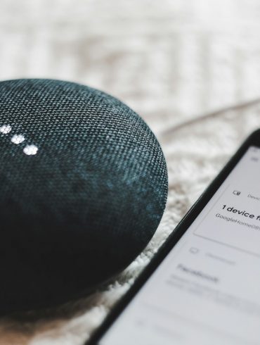 turned-on charcoal Google Home Mini and smartphone