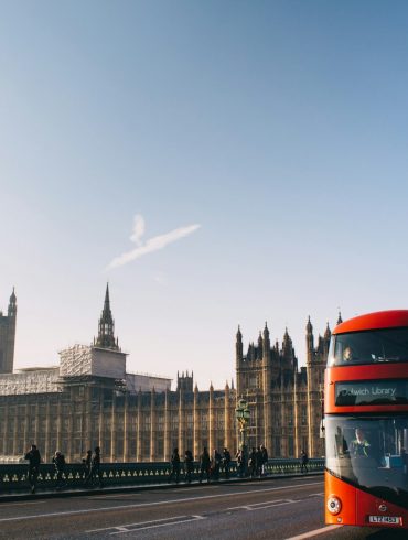 red double-decker bus passing Palace of Westminster, London during daytime