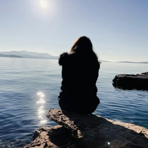 a person sitting on a rock looking out at the water
