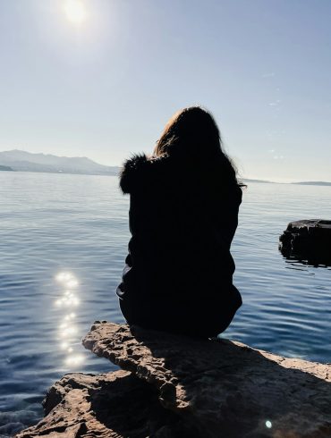 a person sitting on a rock looking out at the water