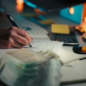 Hand writing in notebook with calculator and cash